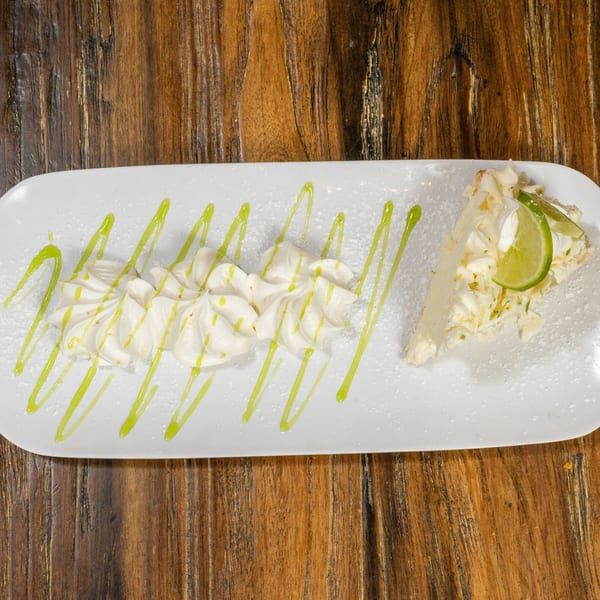 Slice of key lime pie with whipped cream and lime drizzle on a white plate.